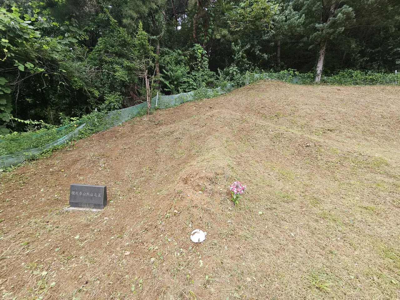 작은 비석과 꽃이 놓인 경사진 봉분, 작업 후